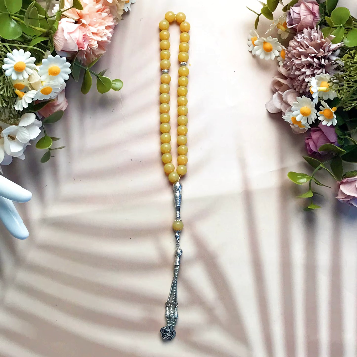 Yellow beaded prayer beads (masbaha) with silver accents on a light pink surface with floral decorations.