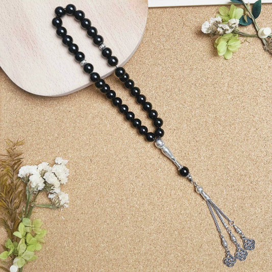 Black beaded prayer beads (masbaha) with silver clasp on a beige surface with flowers