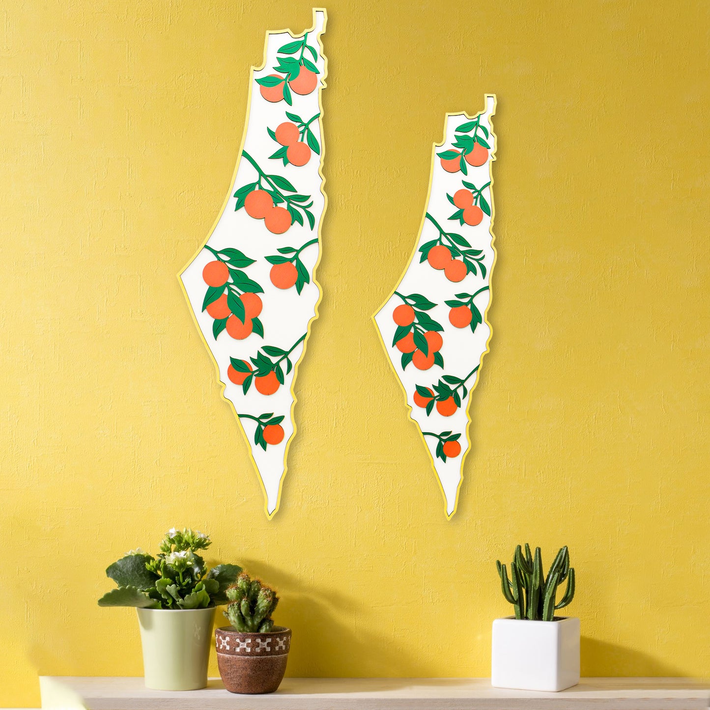 Two decorative wall art pieces shaped like palestine with fruit design on a yellow wall.