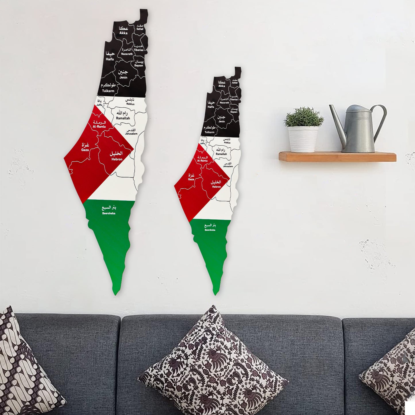 Two wooden wall art pieces shaped like the map of Palestine with flag colors on a white wall above a gray sofa.