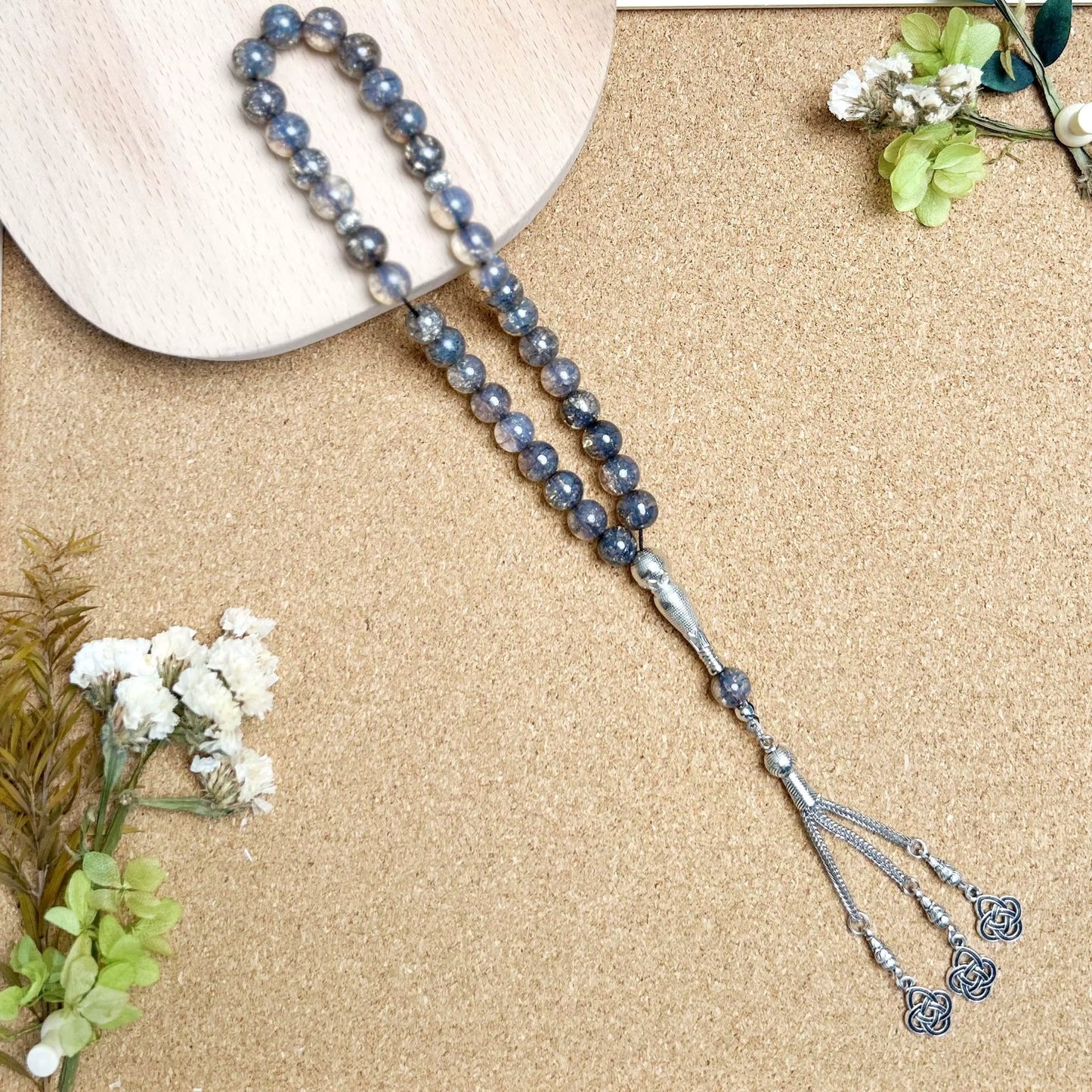 Blue beaded prayer beads (masbaha) with silver tassel on a beige surface with flowers