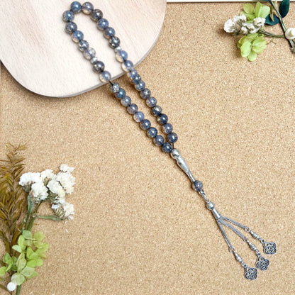 Blue beaded prayer beads (masbaha) with silver tassel on a beige surface with flowers