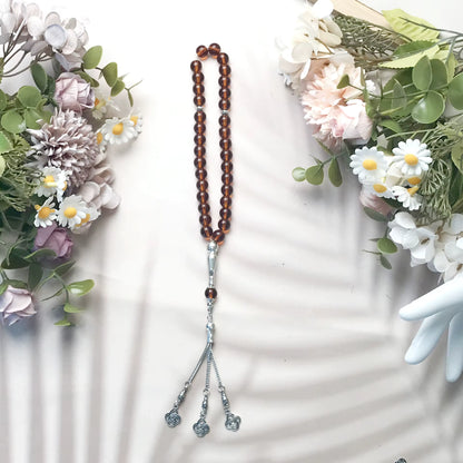 Brown beaded prayer beads with silver accents on a white background with floral decorations