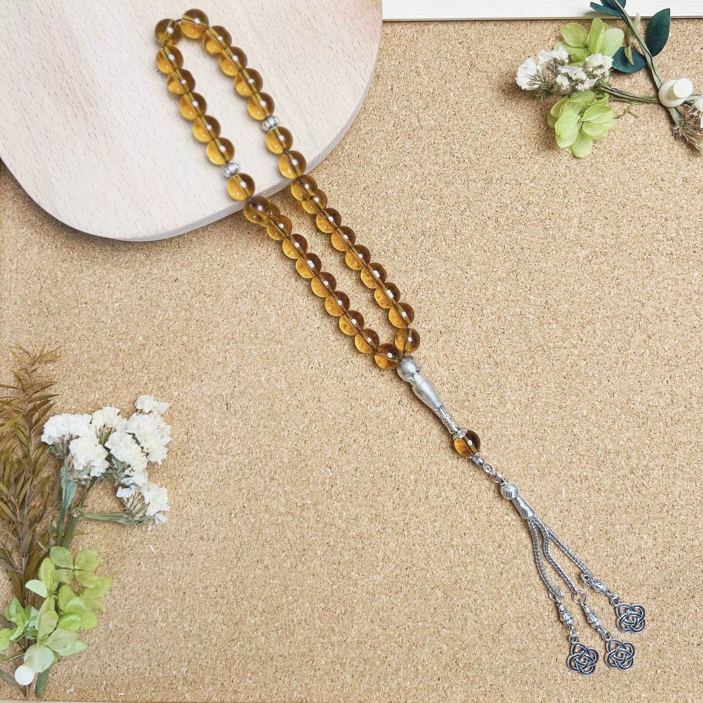 Brown beaded prayer beads (masbaha) with silver tassel on a beige surface with flowers