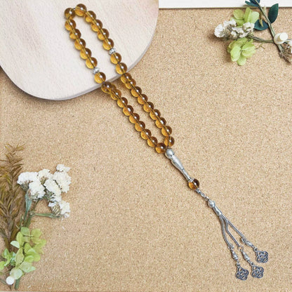 Brown beaded prayer beads (masbaha) with silver tassel on a beige surface with flowers