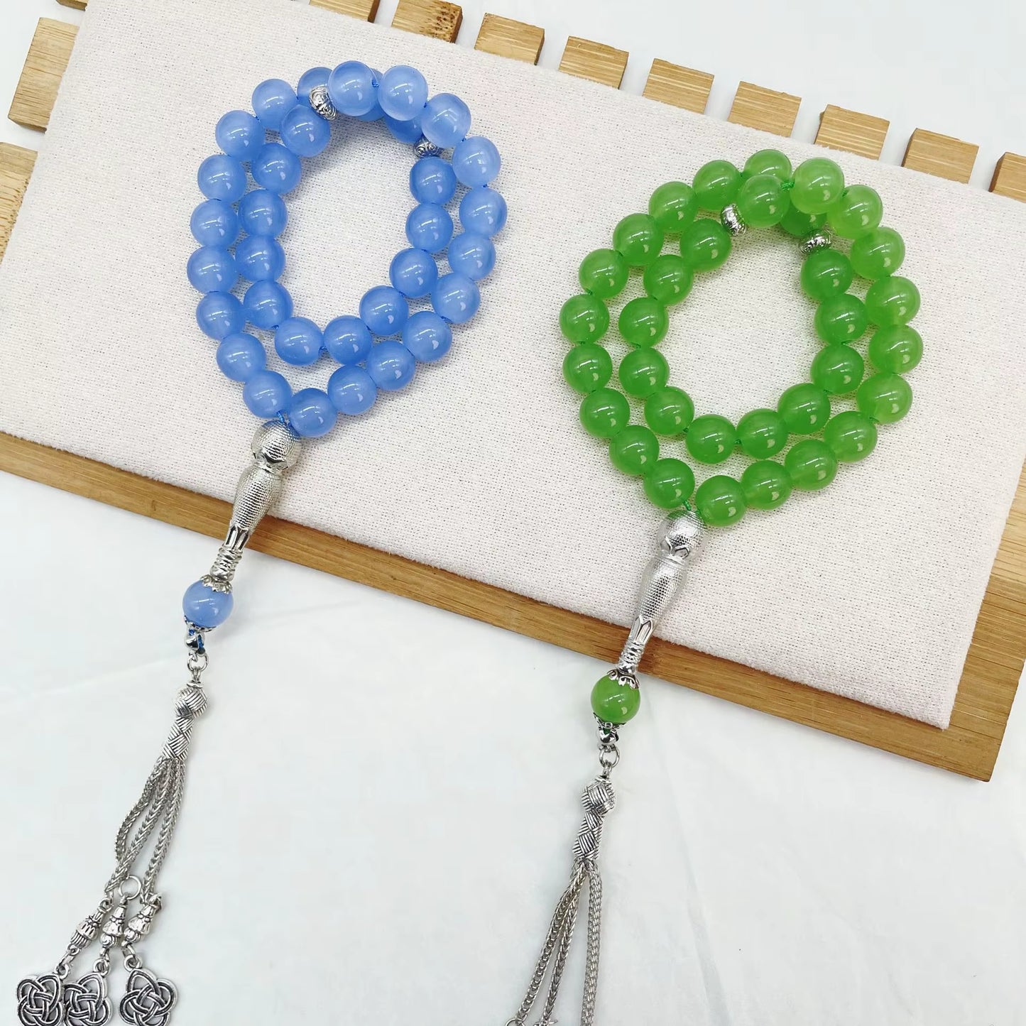 Blue and green beaded prayer beads (masbaha) with silver tassels on a white background