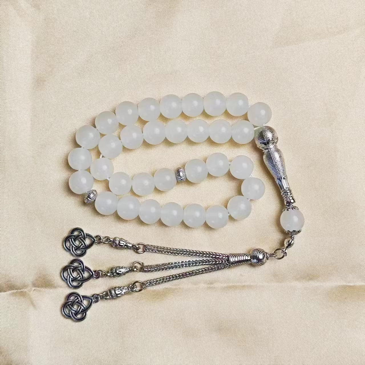 White beaded rosary with prayer beads (masbaha) and finial on a beige background