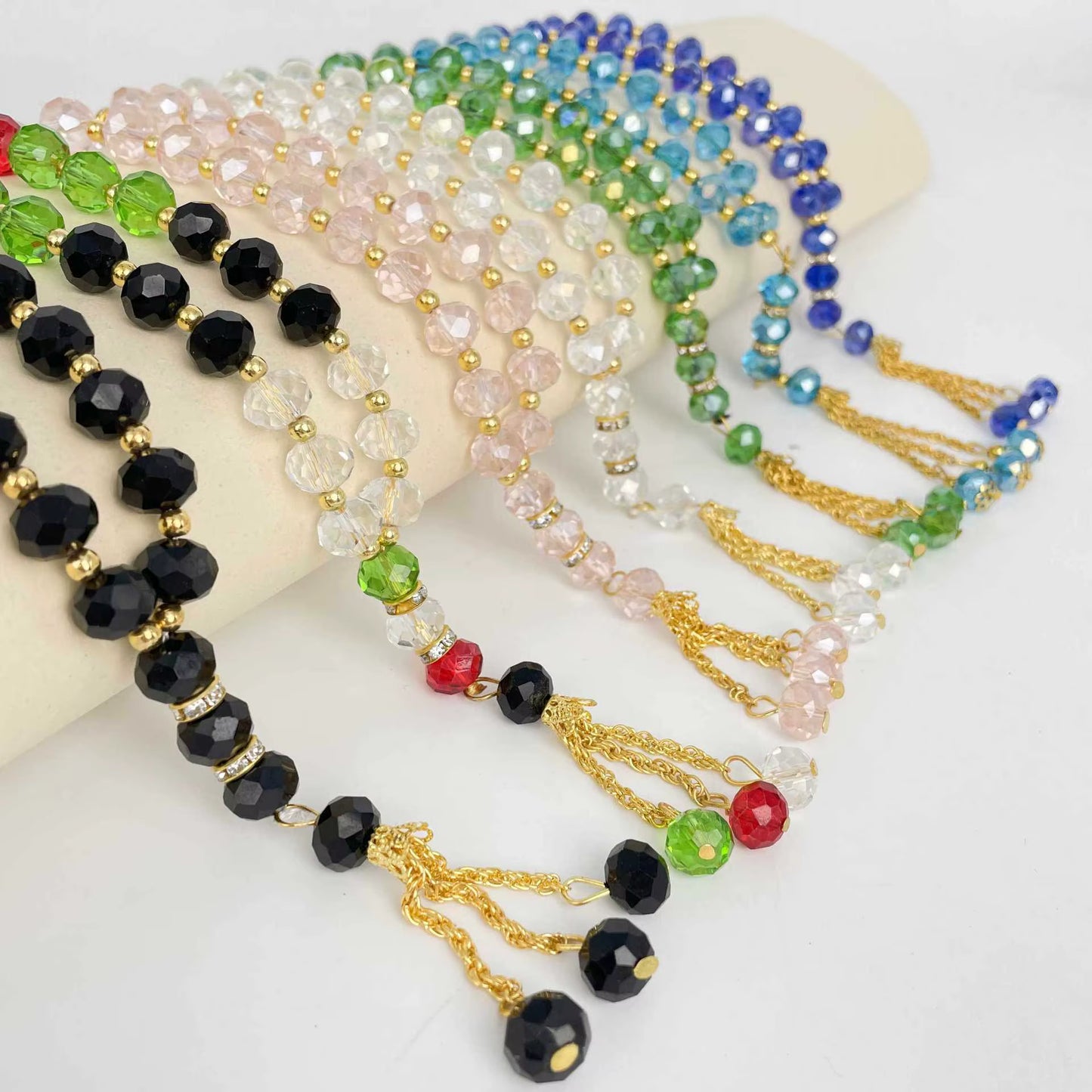 Colorful beaded prayer beads with gold chains on a white surface