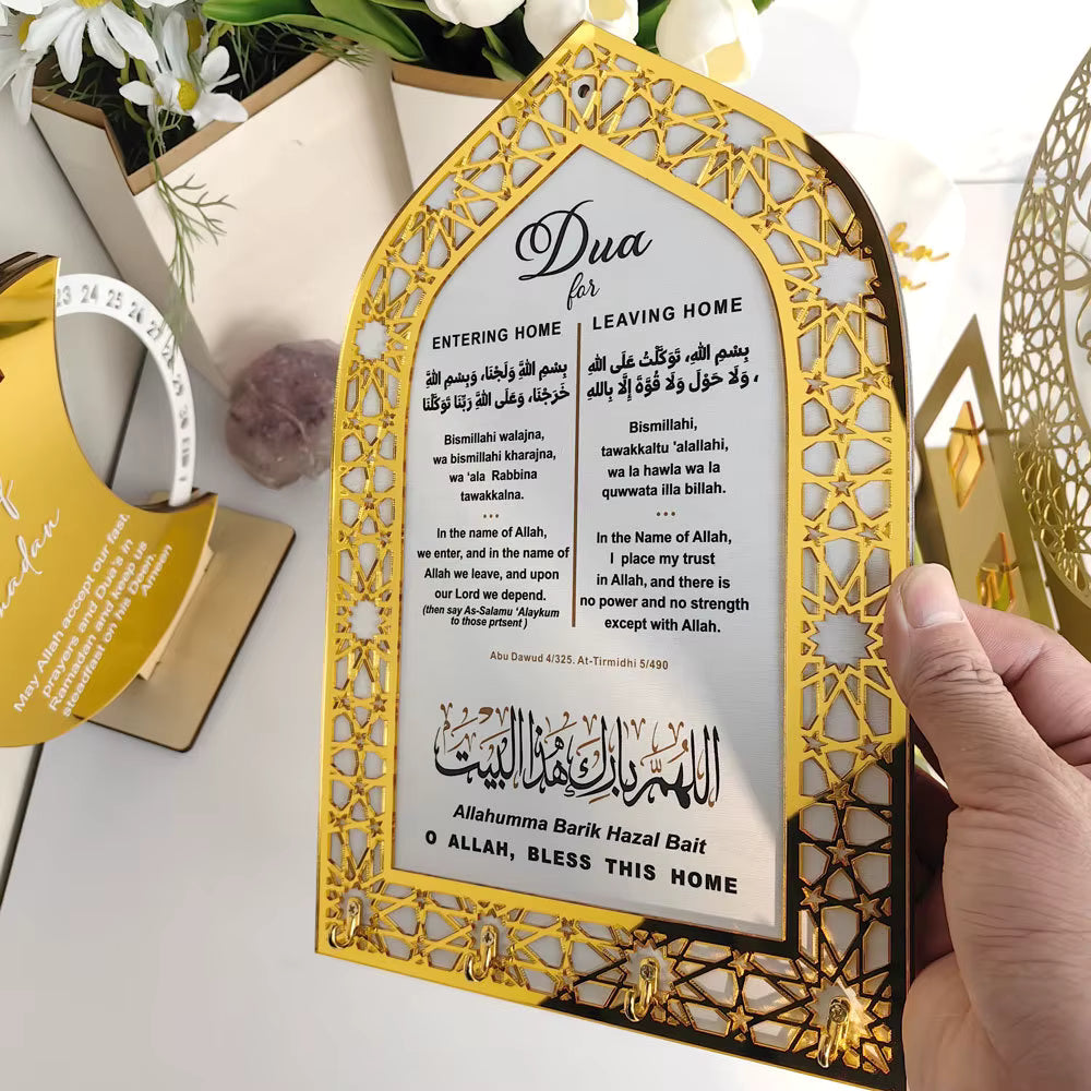Decorative key holder with Arabic text and gold frame held by a hand, with flowers and decor in the background.